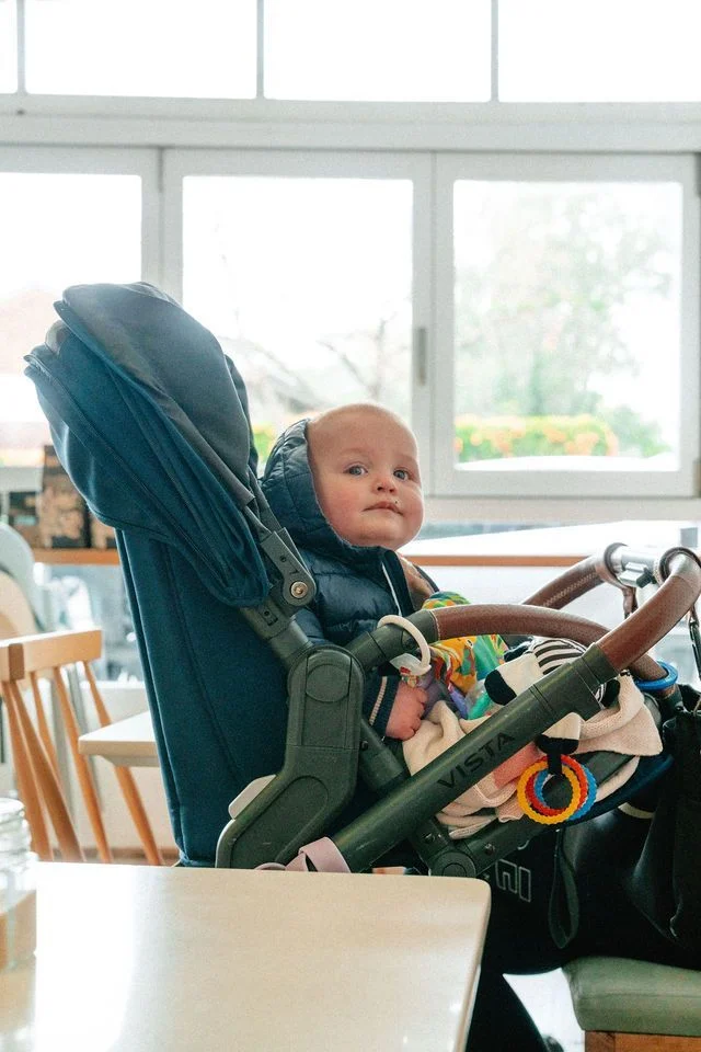 A baby is sitting in a stroller at a table.