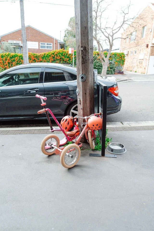 A pink tricycle is parked on the side of the road next to a car.