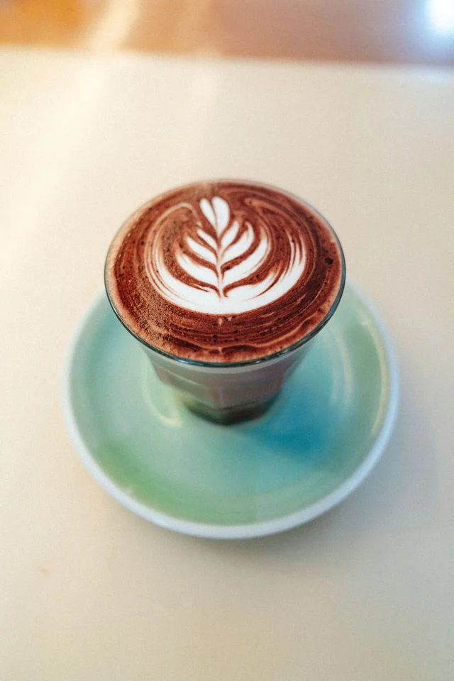 A teal cup of coffee with leaf-shaped latte art
