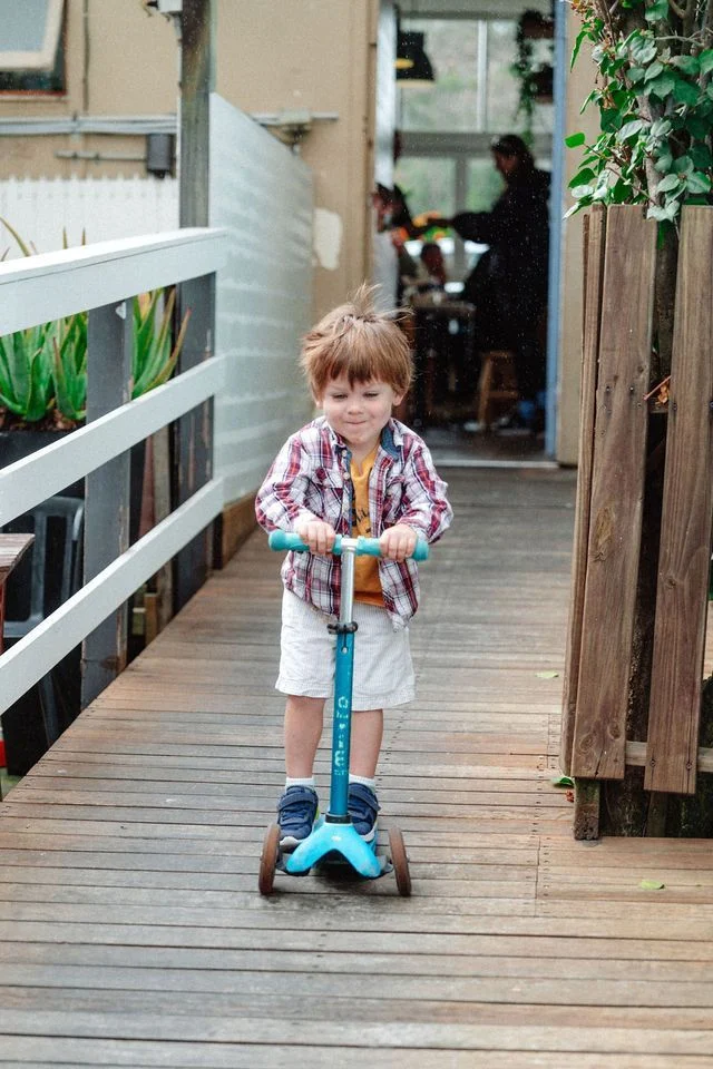 A young boy is riding a scooter on a wooden walkway.