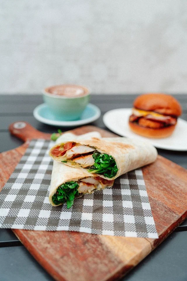 A chicken wrap is sitting on a checkered napkin on a wooden cutting board.