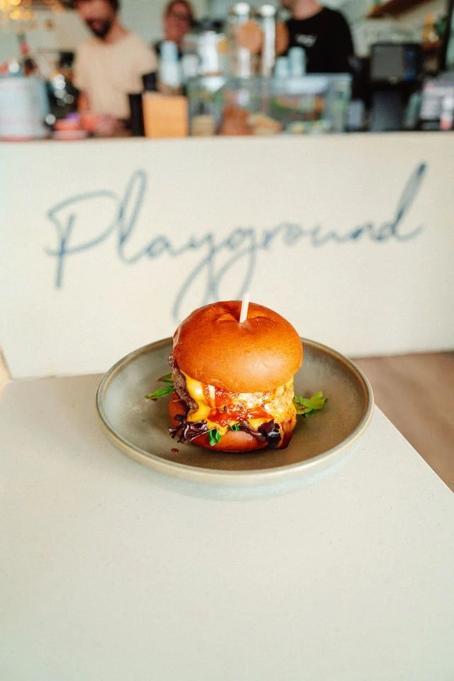 A hamburger with a candle in it is on a plate on a table.