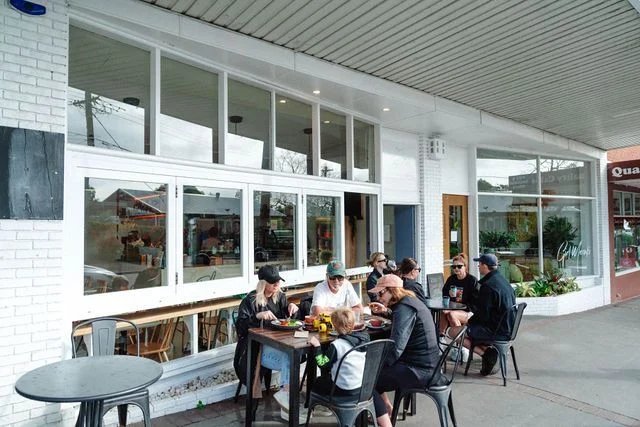 A group of people are sitting at tables outside of a restaurant.
